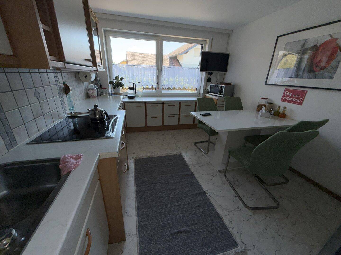 Helle Küche mit Essbereich, Fenster und integrierten Geräten, ideal für gemeinsame Mahlzeiten.