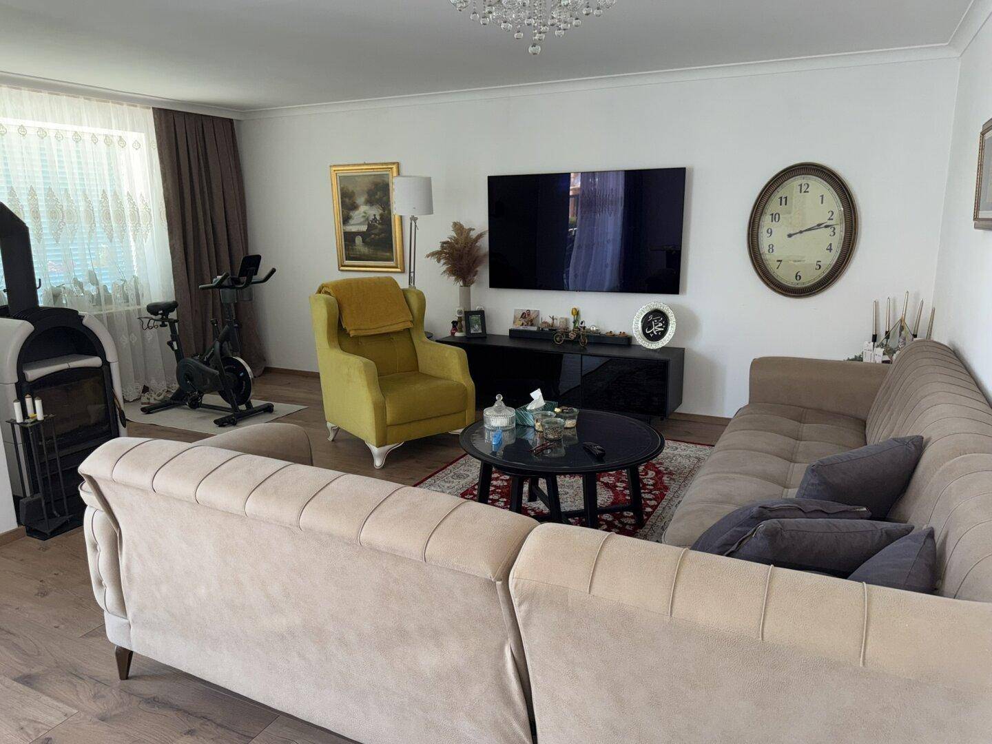 Geräumiges Wohnzimmer mit beigem Sofa, gelbem Sessel und großem Fernseher, ideal zum Entspannen.