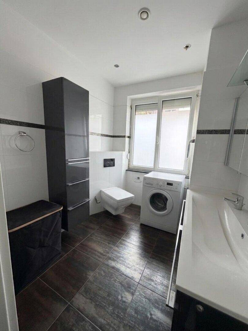Modernes Badezimmer mit Waschmaschine, wandhängendem WC und Fenster.