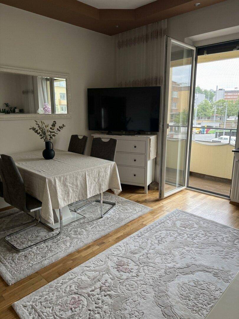 Heller Wohn-Essbereich mit Esstisch, Fernseher und Zugang zum Balkon.