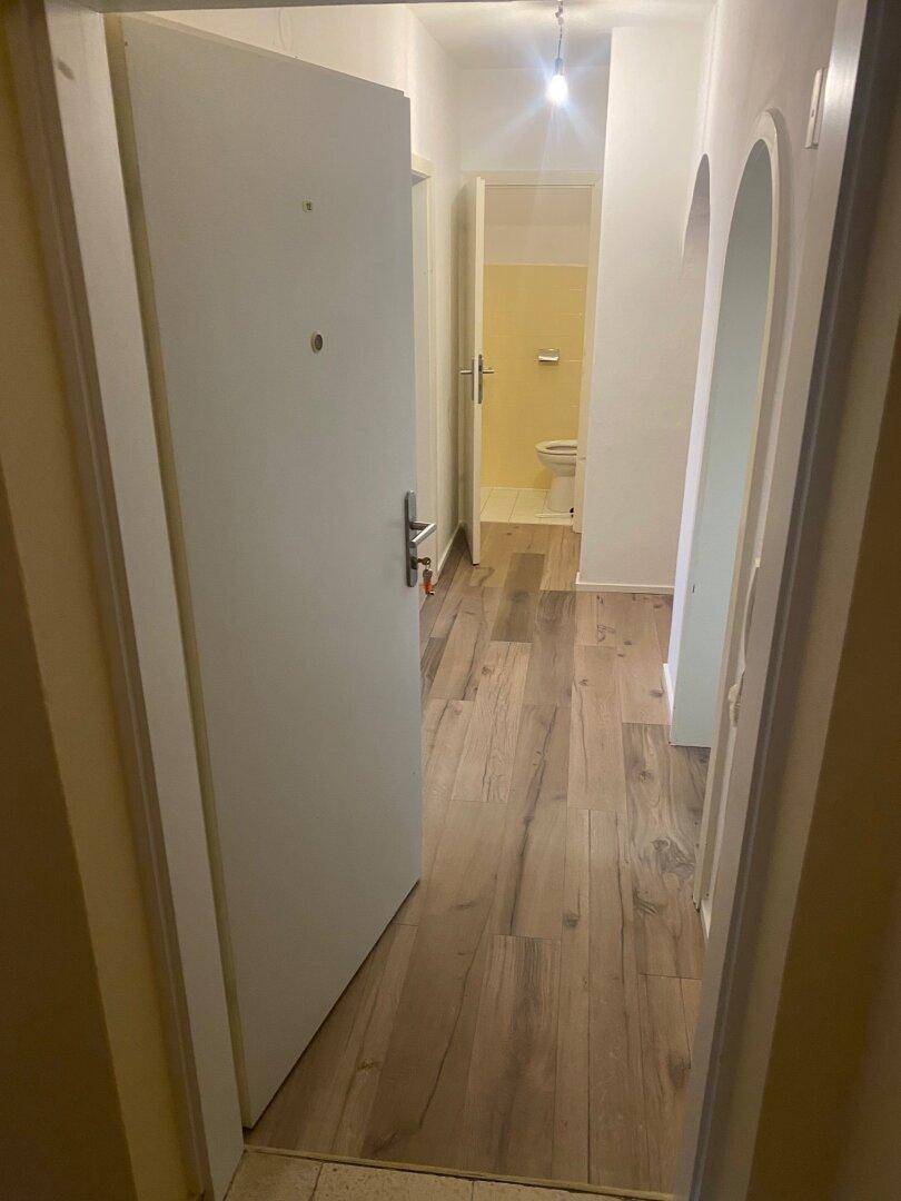 Heller Flur mit Laminatboden, weiß gestrichenen Wänden und einer bogenförmigen Tür, die zu weiteren Räumen führt.