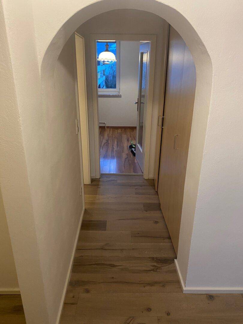 Langer Flur mit Laminatboden und weiß gestrichenen Wänden, der durch einen Bogen zu weiteren Räumen führt.