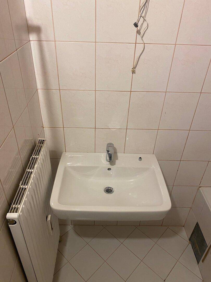 Kleines WC mit weißen Fliesen, einem Waschbecken und einem Heizkörper, in gutem Zustand.