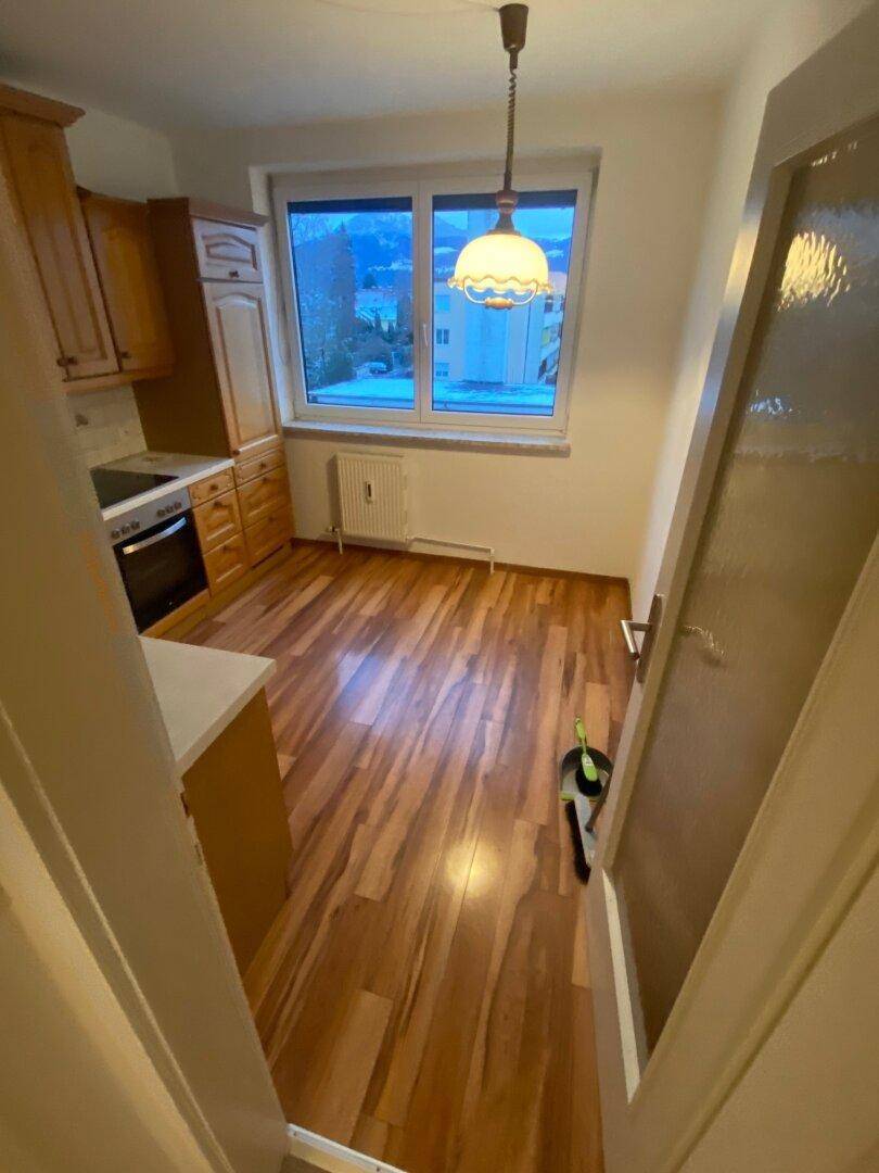 Küche mit Fenster und Blick auf verschneite Bäume und Gebäude, ausgestattet mit Holzschränken und Laminatboden.