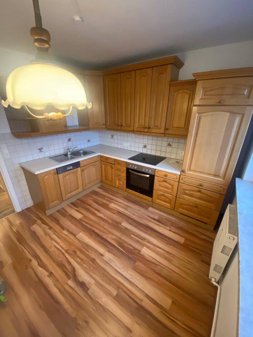 Funktionale Küche mit Holzschränken, weißer Arbeitsplatte und integrierten Geräten, ausgestattet mit Laminatboden.