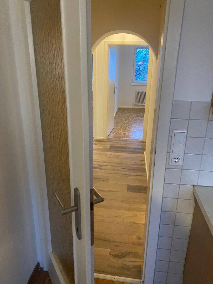 Blick von einem Eingangsbereich in einen Flur mit Laminatboden, der zu einem weiteren Zimmer führt.