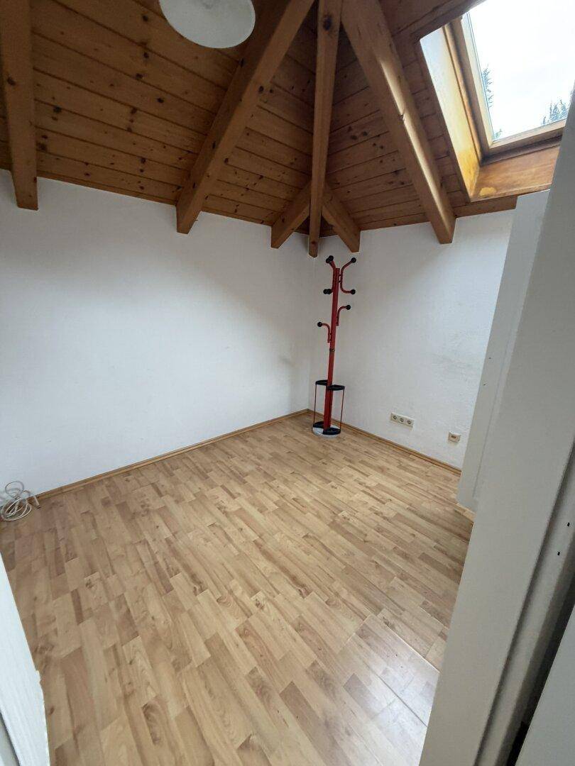 Dachzimmer mit Holzbalken, Dachfenster und Laminatboden, ideal als Schlaf- oder Arbeitszimmer.
