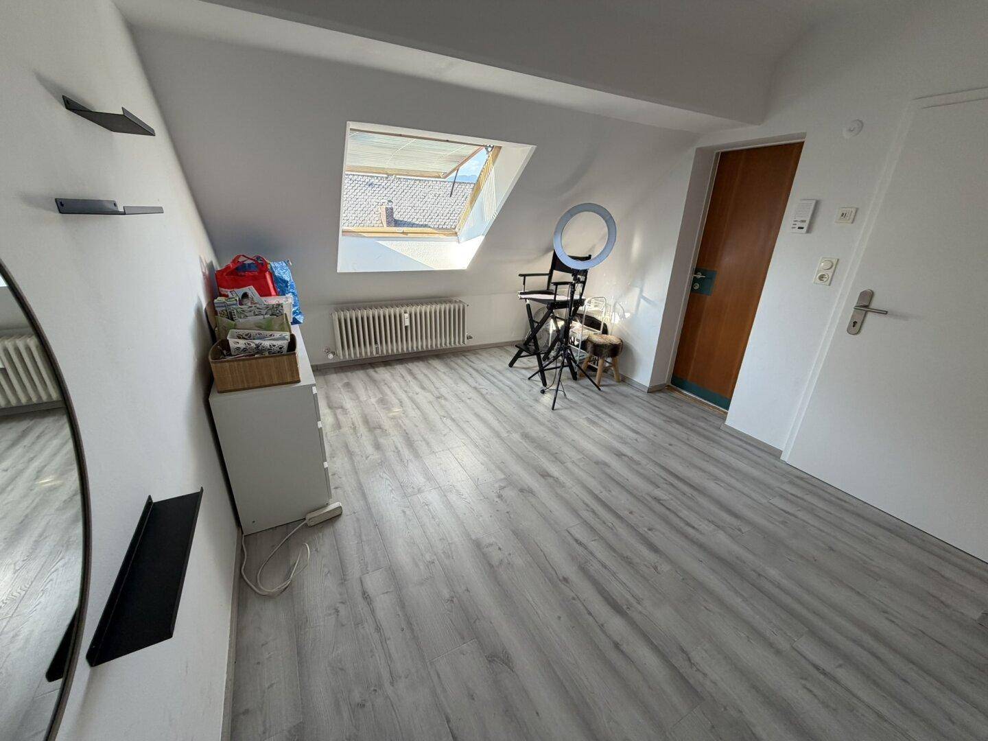 Geräumiges Dachzimmer mit Laminatboden, Dachfenster und Holztür.