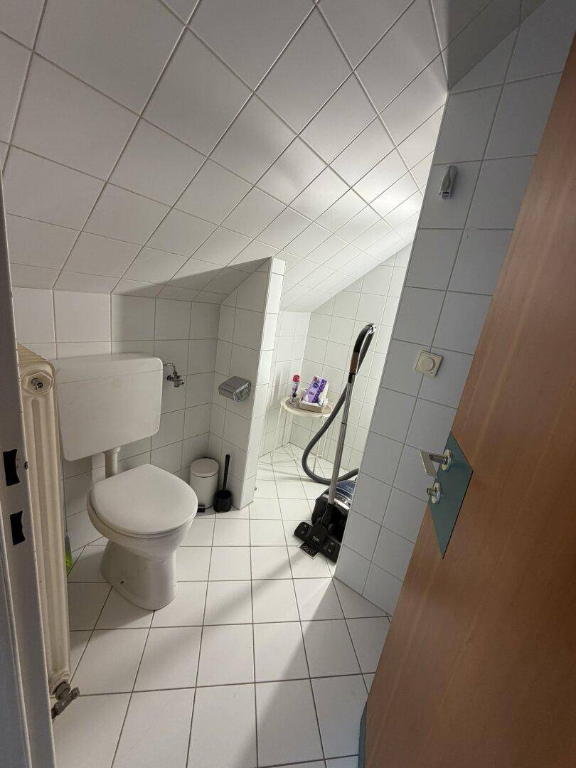 Gefliestes Badezimmer mit Toilette, Heizkörper und Schrägdach.
