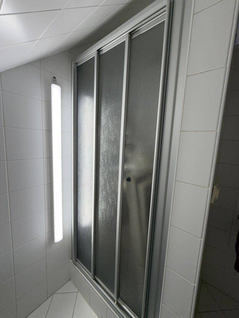 Duschkabine mit Milchglas-Schiebetüren im gefliesten Badezimmer.