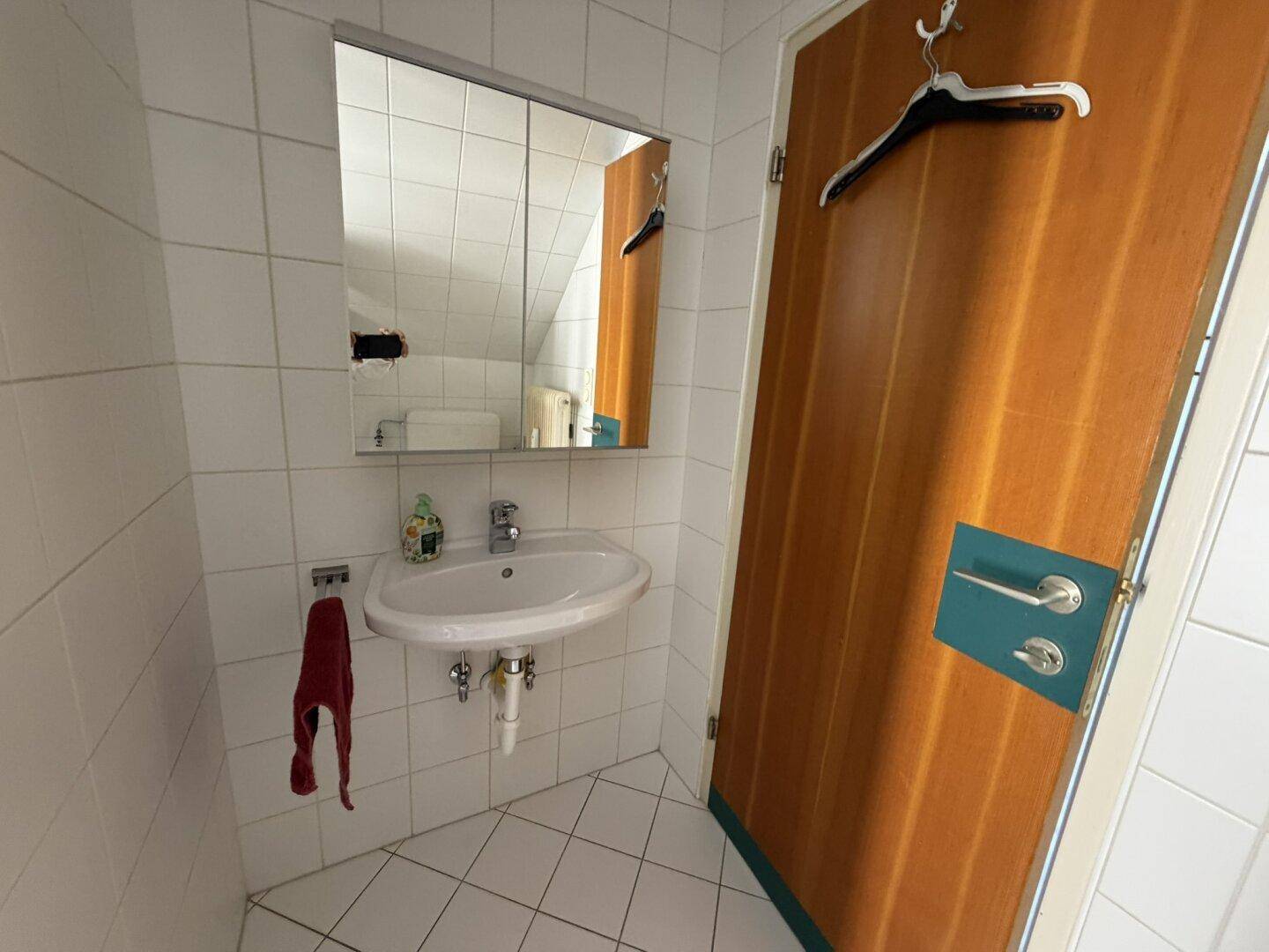 Badezimmer mit Waschbecken, Spiegelschrank und weißen Wandfliesen.