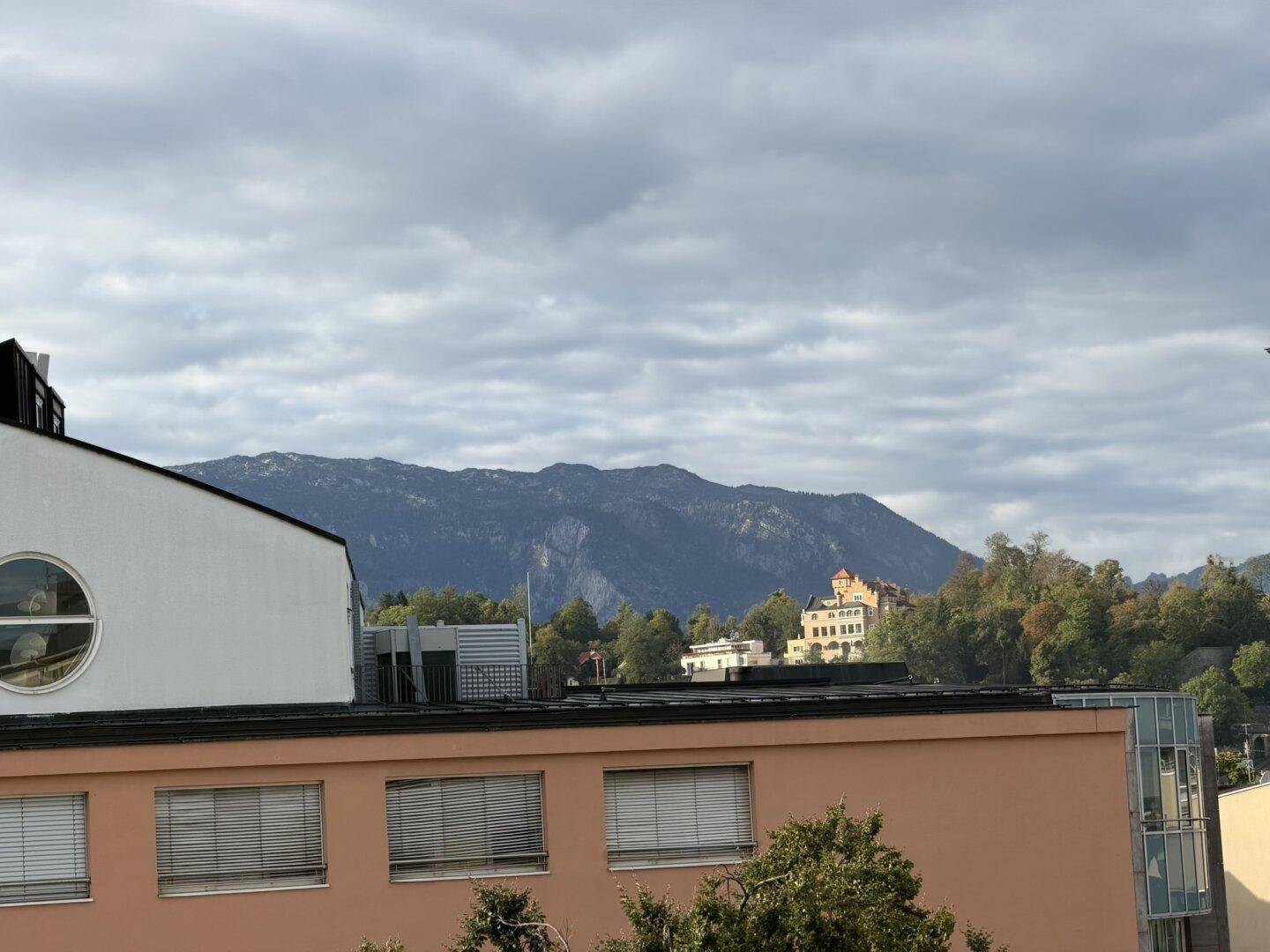 Panoramablick auf die umliegende Berglandschaft und historische Gebäude unter bewölktem Himmel.