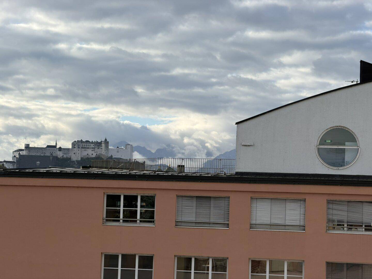 Weitblick auf die Festung Hohensalzburg und die Stadtkulisse unter bewölktem Himmel.