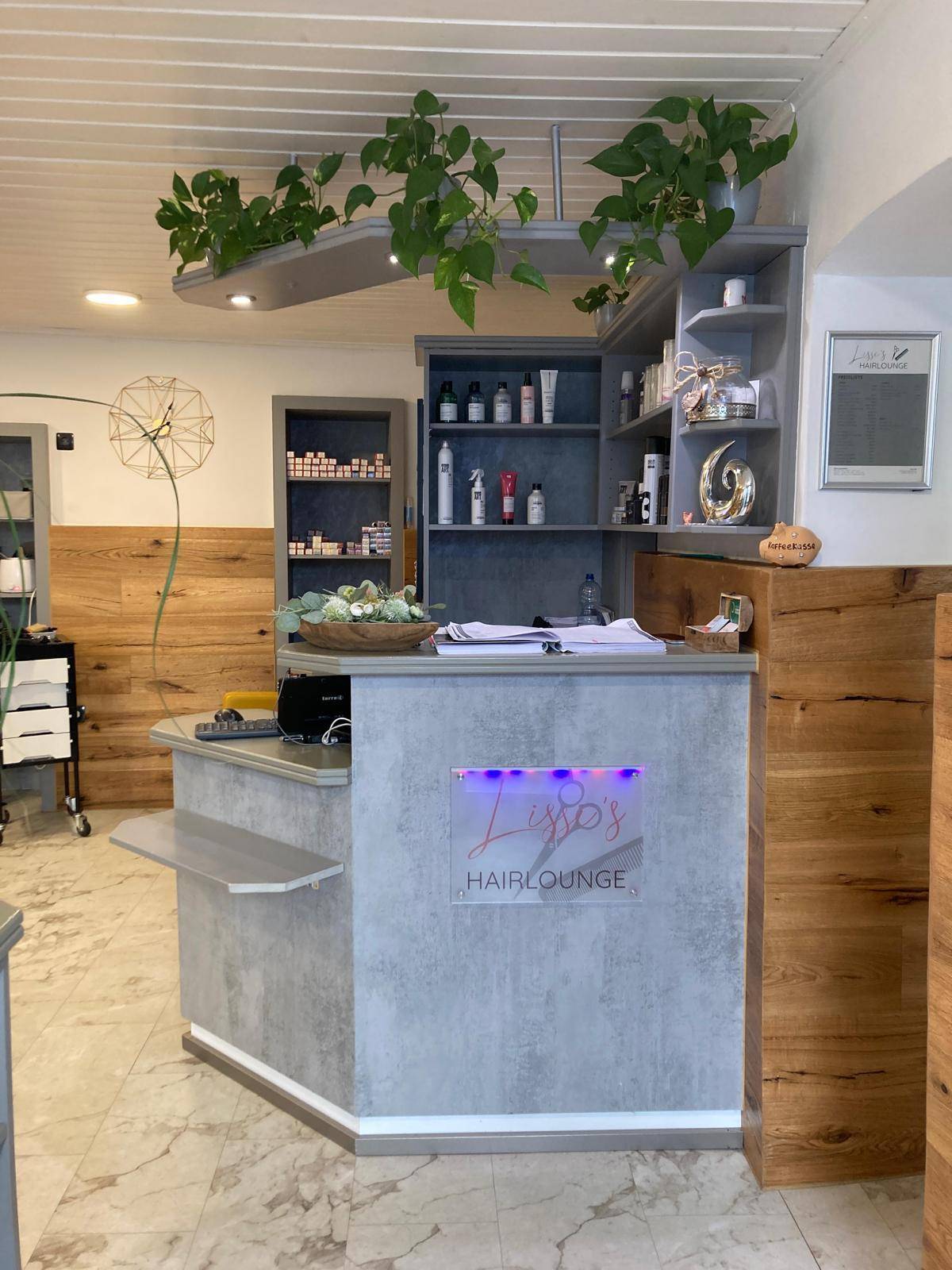 Empfangsbereich eines Salons mit moderner Theke, Regalen und Pflanzen, gut beleuchtet.
