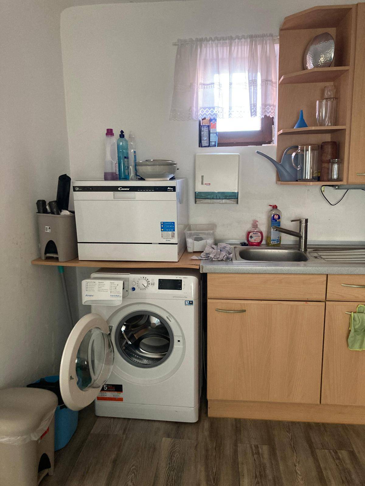 Kleine Küche mit Waschmaschine, Geschirrspüler und Spüle unter einem Fenster.