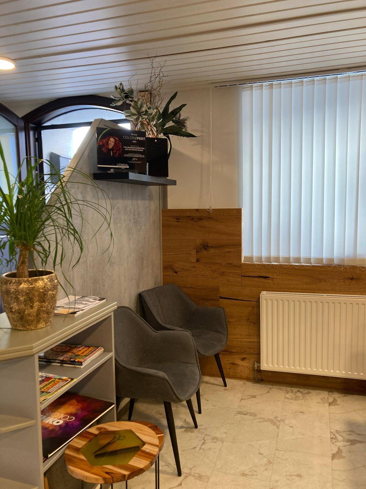 Gemütlicher Wartebereich mit zwei grauen Sesseln, Fenster und Pflanzen, in einem Salon.