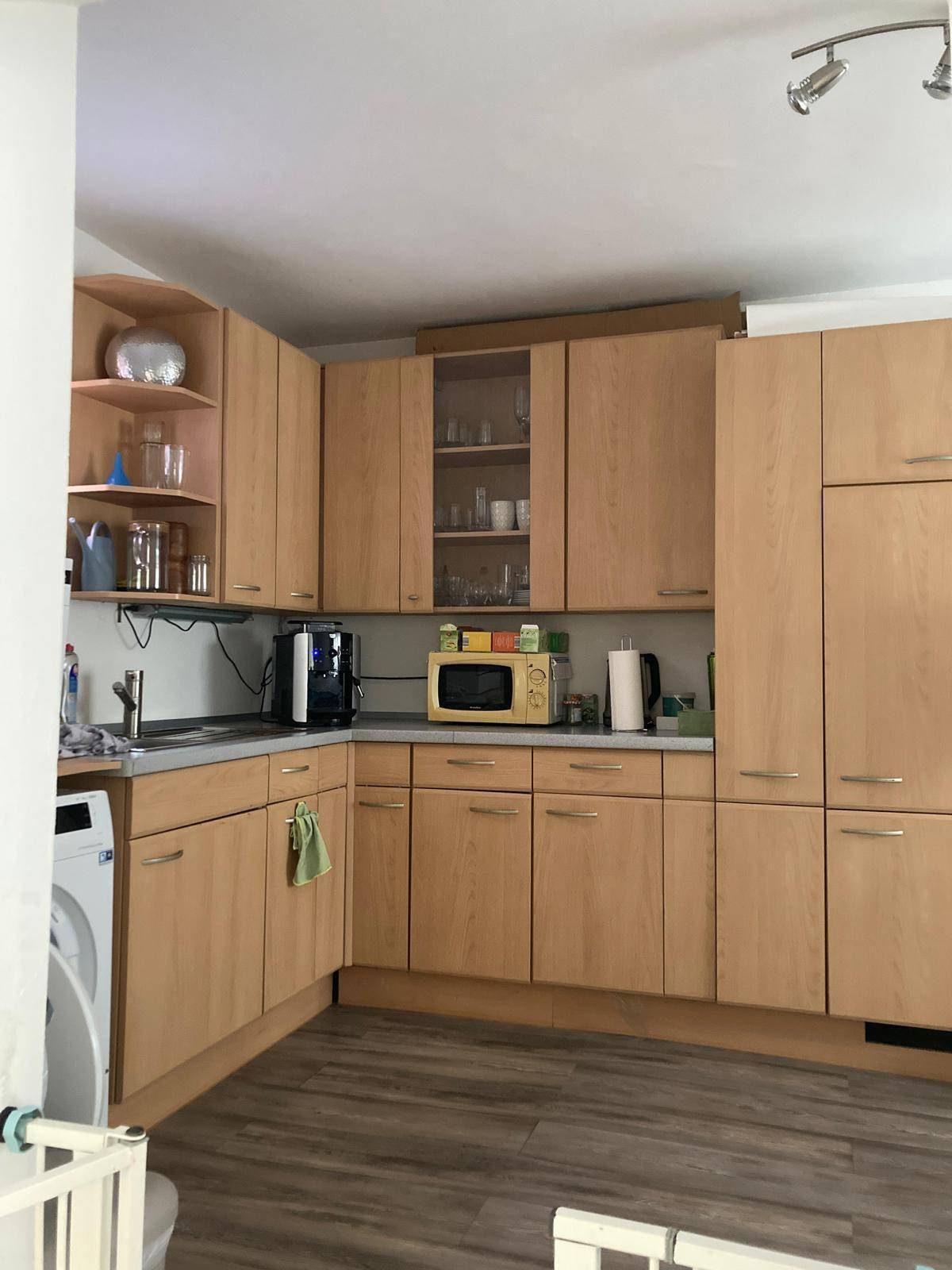 Funktionale Küche mit hellen Holzschränken, Mikrowelle und Spüle, mit dunklem Boden.