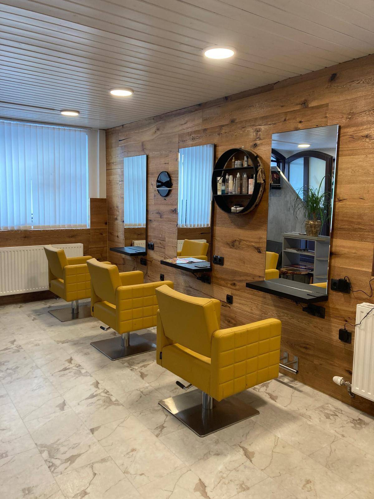 Geräumiger Friseursalon mit mehreren Arbeitsplätzen, Holzvertäfelung und Fliesenboden.