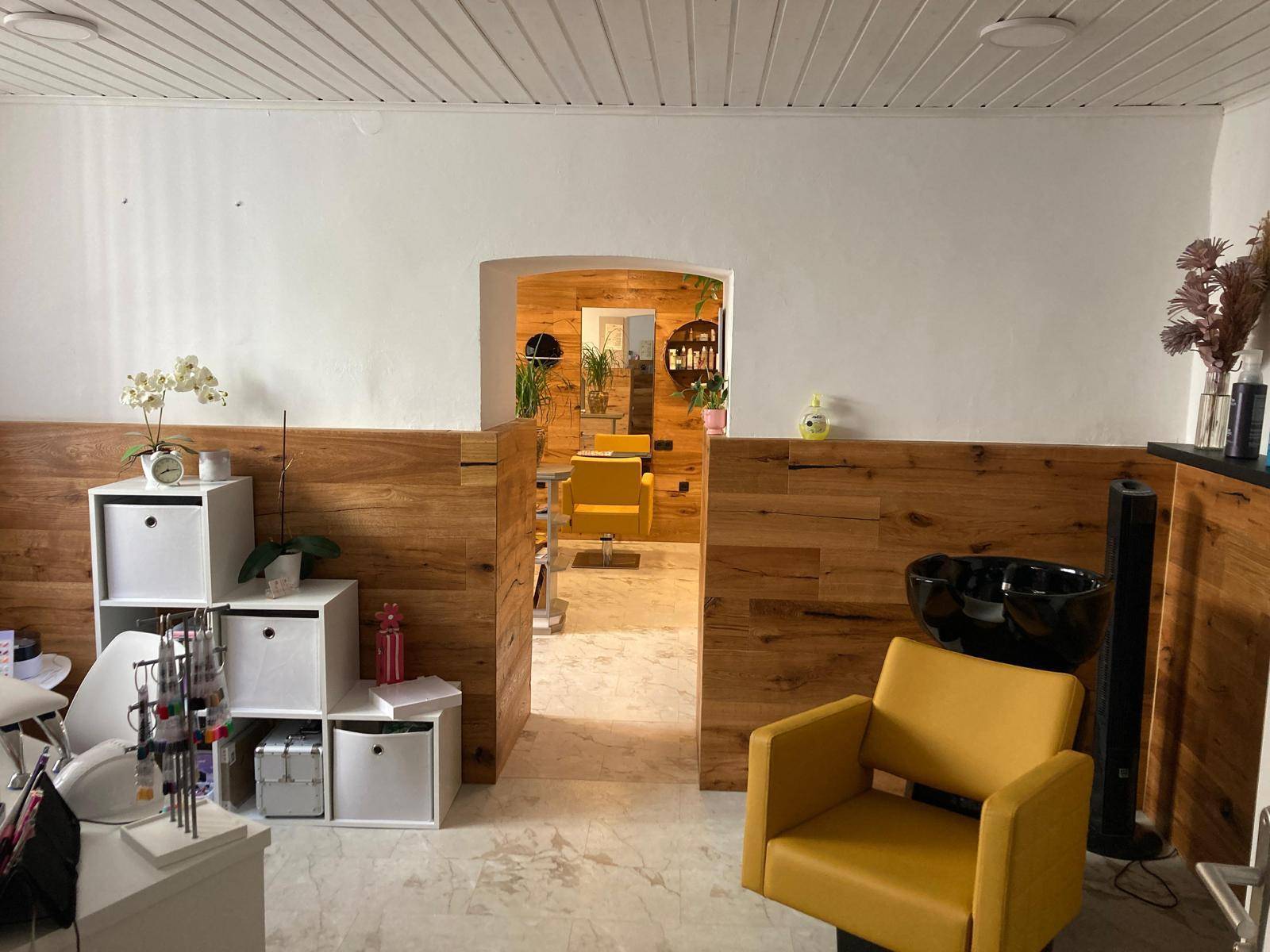 Blick durch einen Bogen in den Hauptsalonbereich mit gelben Stühlen und Holzvertäfelung.