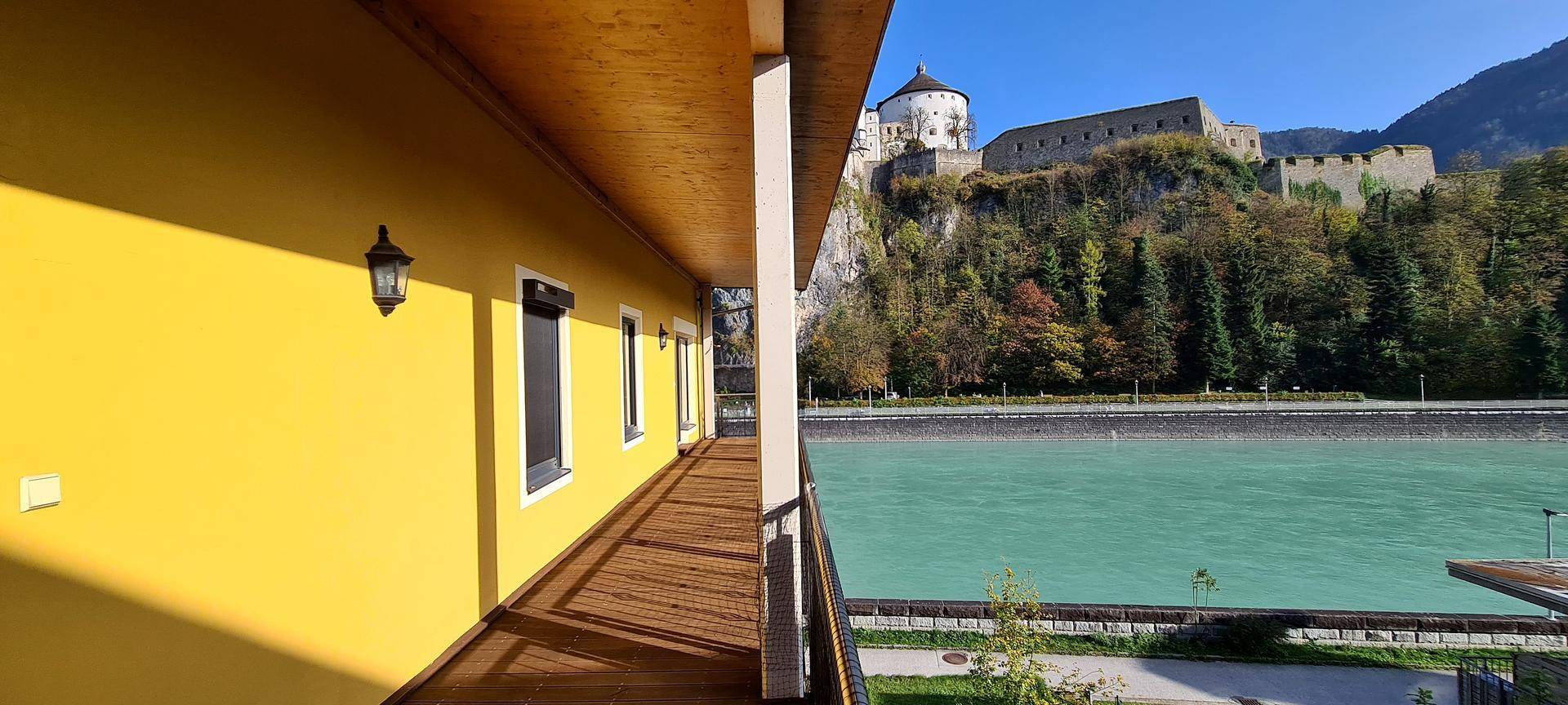 Langer Balkon mit gelber Fassade und Blick auf den Fluss sowie die historische Festung.