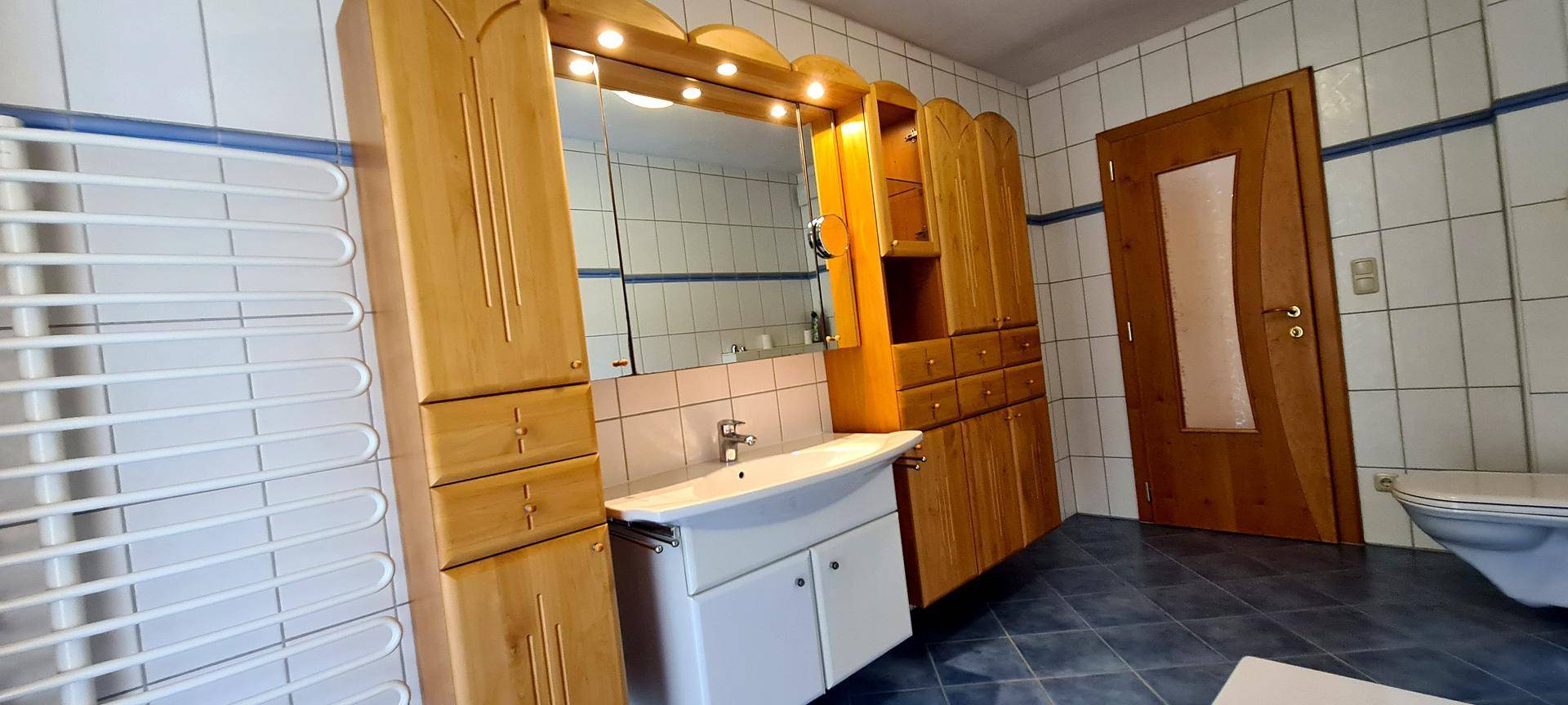 Badezimmer mit Einzelwaschbecken, Spiegelschrank und Holzmöbeln.
