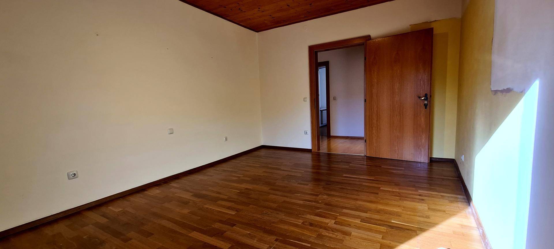 Helles Schlafzimmer mit Parkettboden und Holzbalkendecke, bereit zur Einrichtung.
