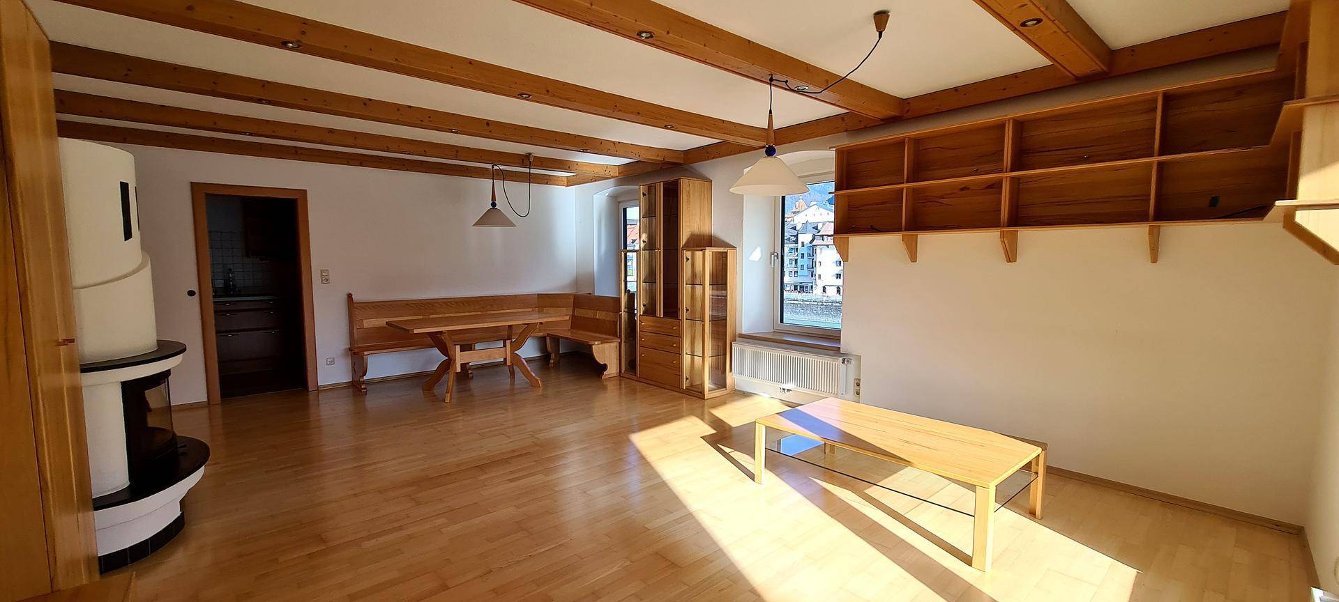 Geräumiges Wohn- und Esszimmer mit Holzbalkendecke, Parkettboden und traditionellem Kachelofen.