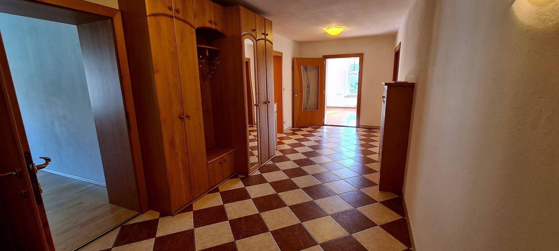 Flur mit Schachbrettmuster-Fliesenboden und Holzschrank, der zu weiteren Räumen führt.