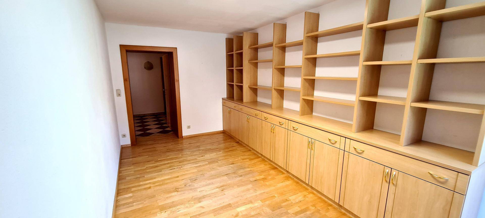 Geräumiges Arbeitszimmer mit umfangreichen Holzregalen und Parkettboden.