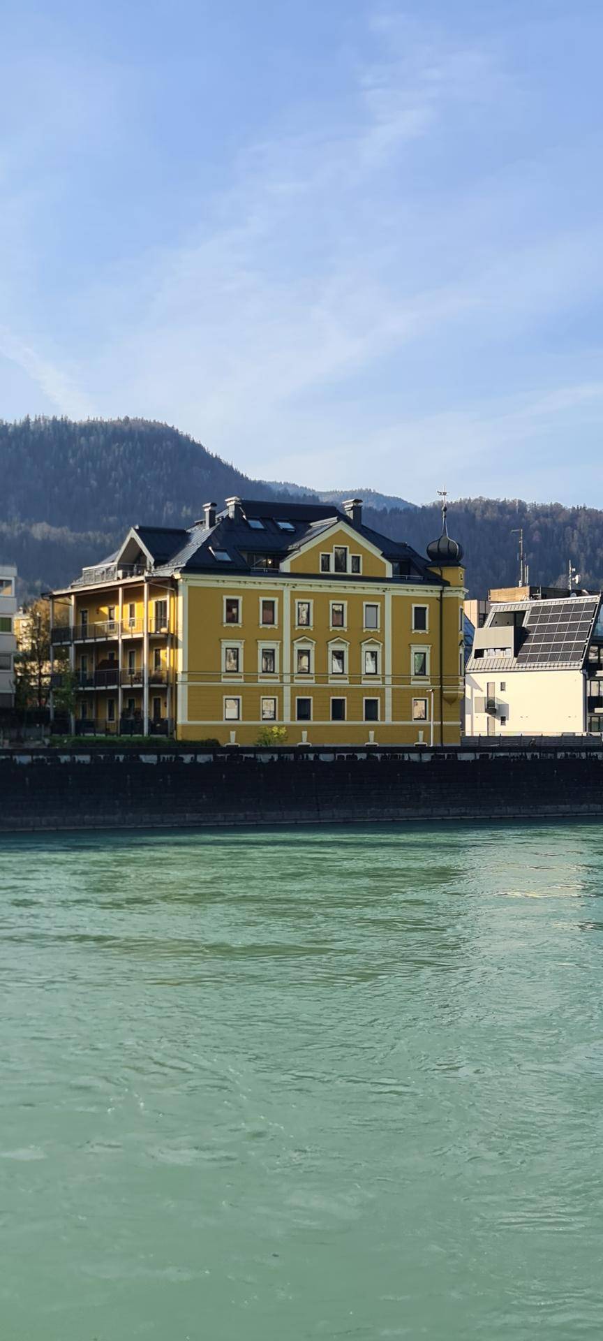 Gelbes Gebäude am Flussufer mit traditioneller Architektur und Bergblick.