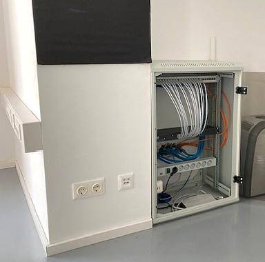 Technikraum mit Server-Rack, Verkabelung und zahlreichen Steckdosen für IT-Infrastruktur.