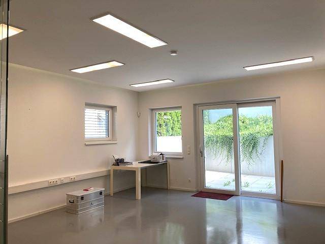 Geräumiger Büroraum mit effizienter Deckenbeleuchtung, großen Fenstern und Zugang zur Terrasse.