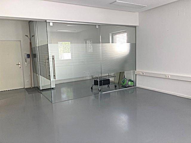 Moderner Bürobereich mit Glaswand und grauem Boden, ideal für flexible Arbeitsplatzgestaltung.