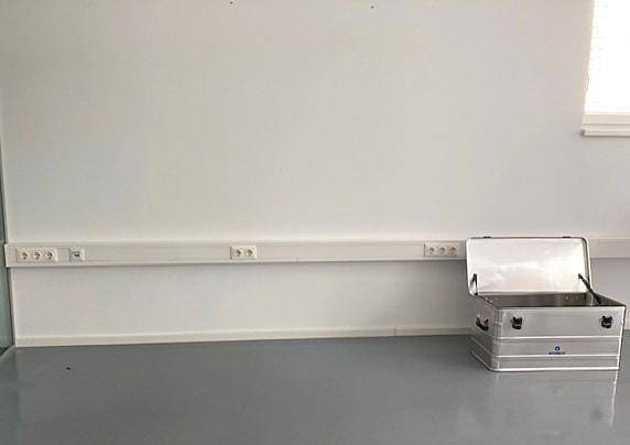 Wandbereich in einem Büroraum mit durchgehender Steckdosenleiste und einem Aluminiumkoffer.