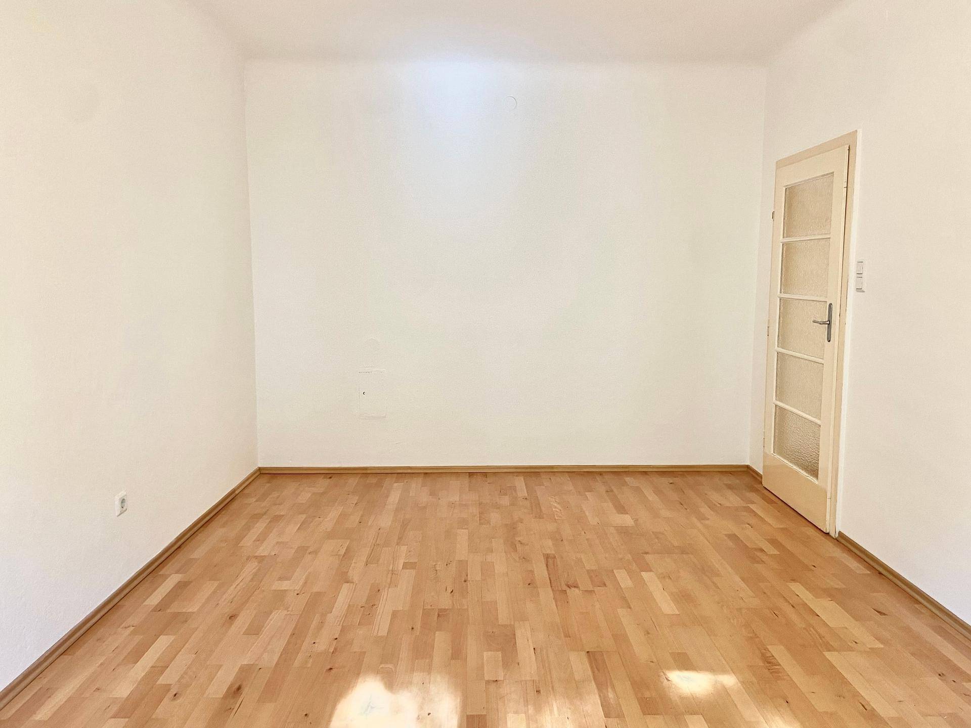 Leeres Zimmer mit hellem Parkettboden und einer Tür mit Glaseinsätzen.