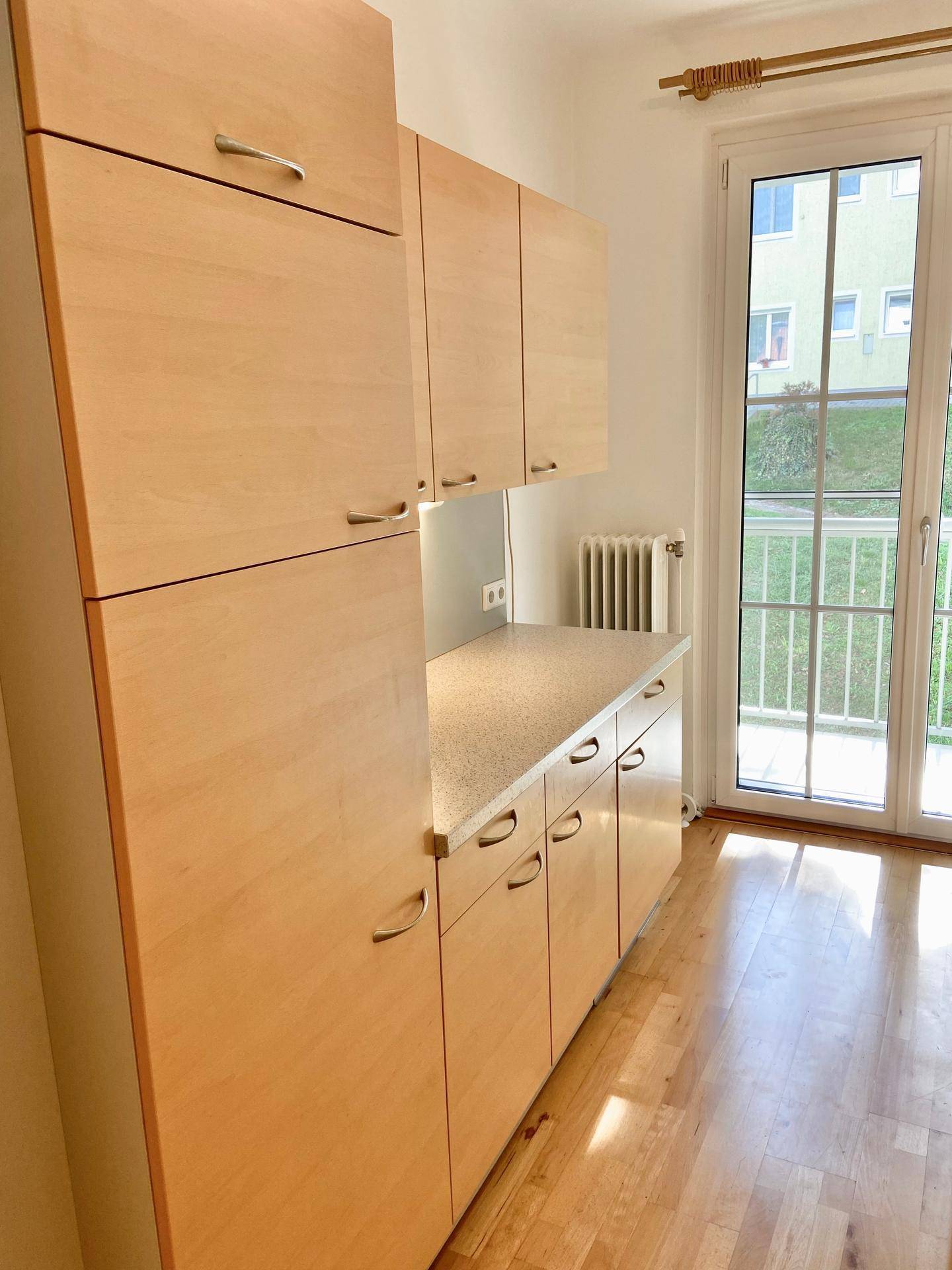 Küchenschränke aus hellem Holz mit Arbeitsplatte und Zugang zu einem Balkon.