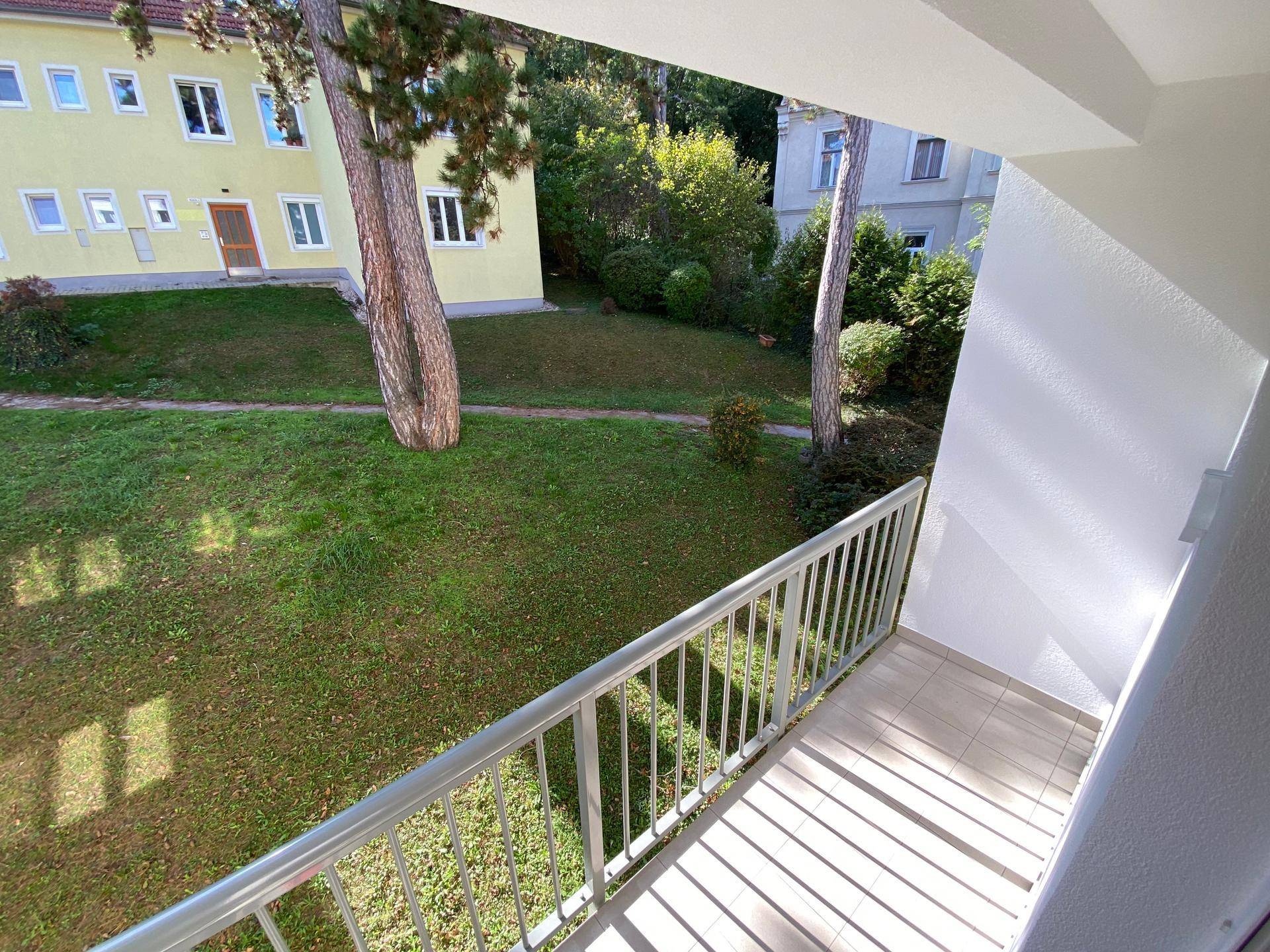 Blick vom Balkon auf den grünen Gartenbereich und die umliegenden Gebäude.