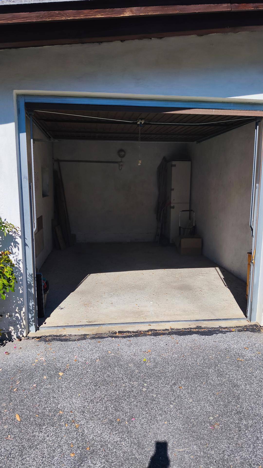 Nahaufnahme der offenen Garage mit Betonboden und einfacher Ausstattung unter hellem Sonnenlicht.