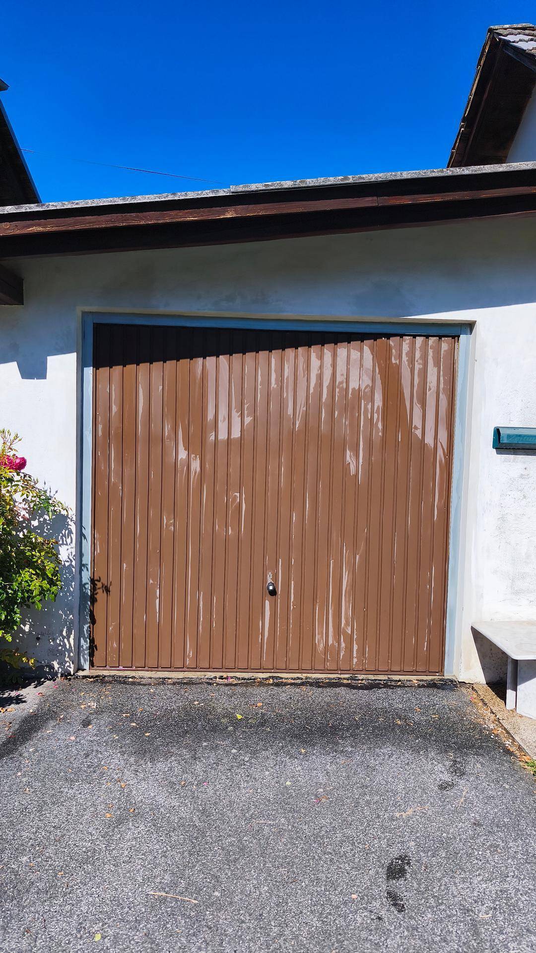 Geschlossenes, braunes Garagentor mit sichtbaren Gebrauchsspuren und asphaltierter Einfahrt.