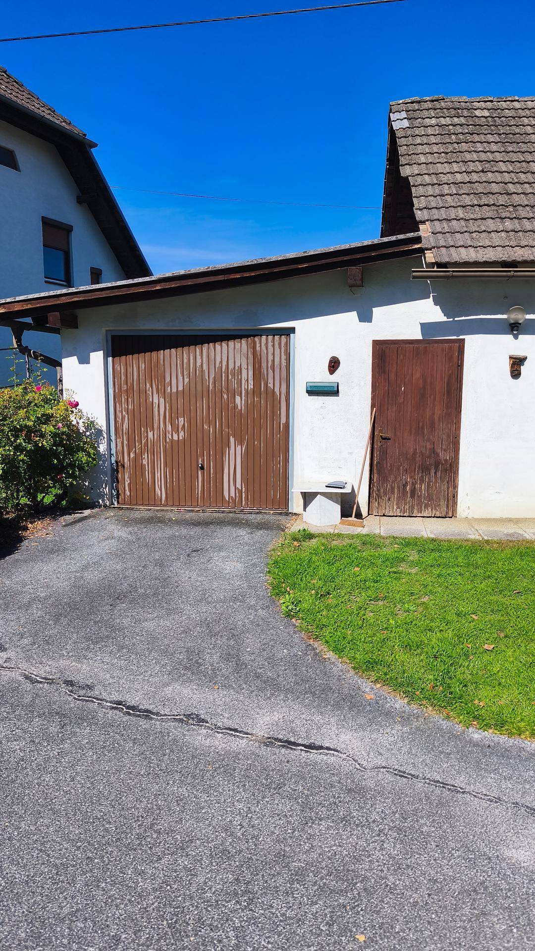 Garagengebäude mit braunem Tor, Holztür, asphaltierter Einfahrt und gepflegter Rasenfläche.