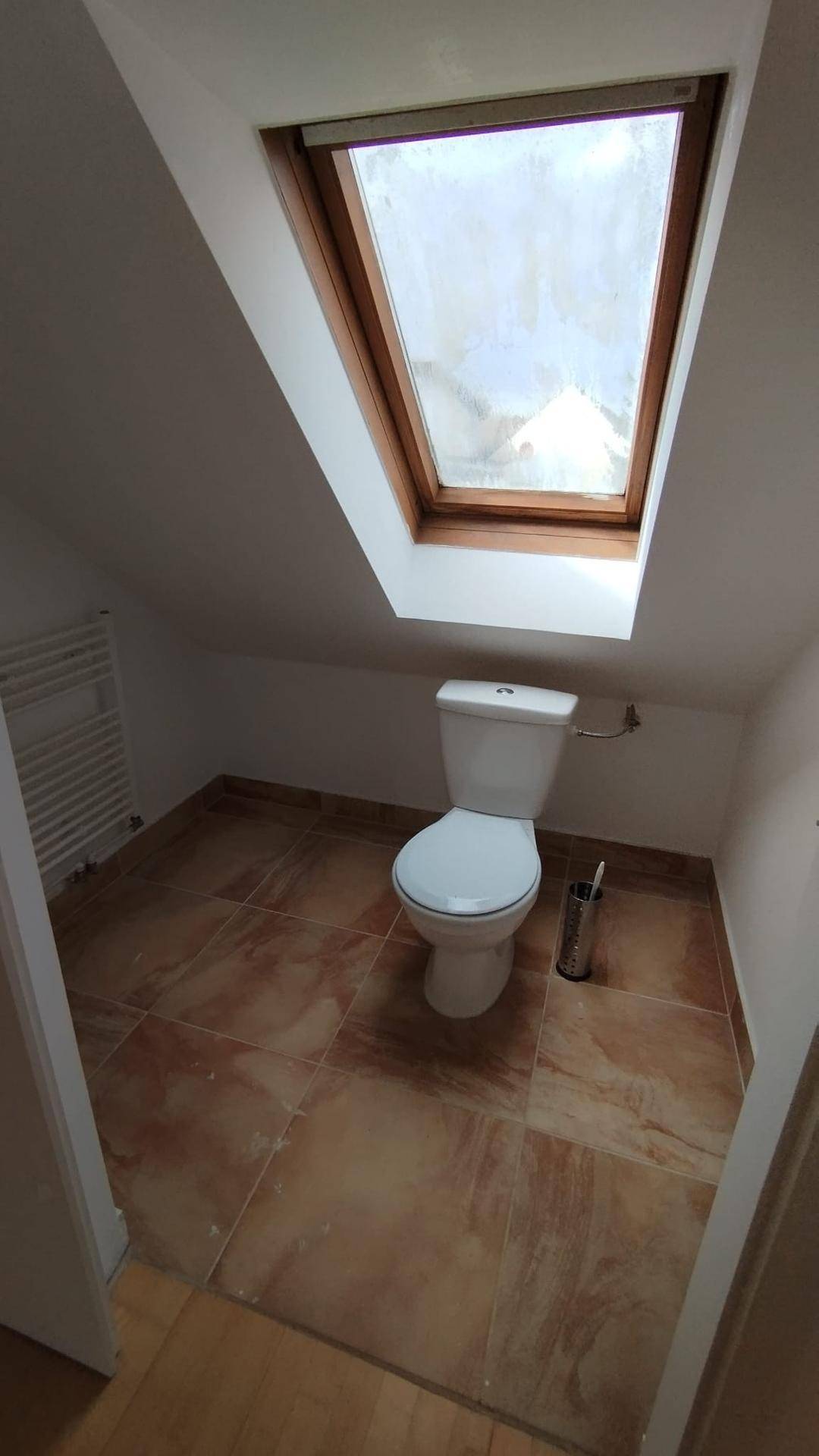 Dachgeschoss-WC mit schrägen Wänden, Fliesenboden und einem Dachfenster für Tageslicht.