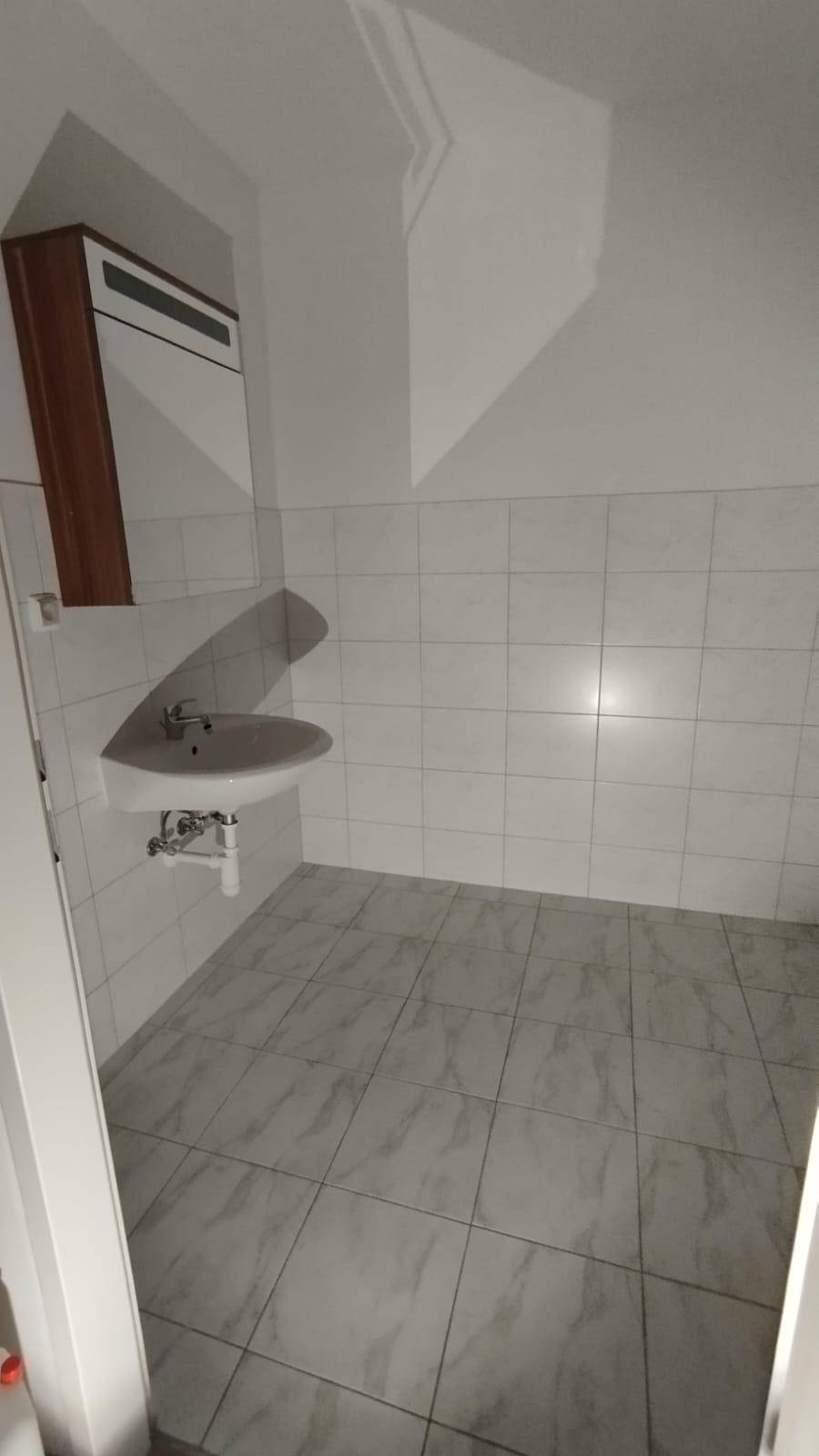 Badezimmer mit hellen Fliesen, einem Waschbecken und einem Spiegelschrank.