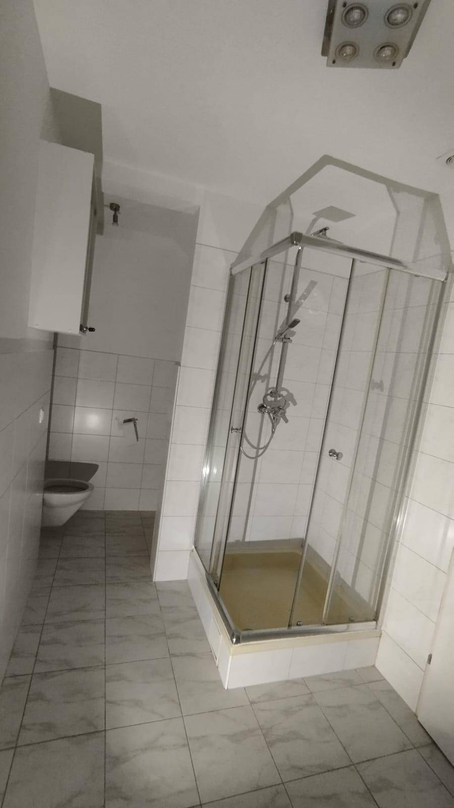 Badezimmer mit Duschkabine, WC und hellen Fliesen an Wänden und Boden.