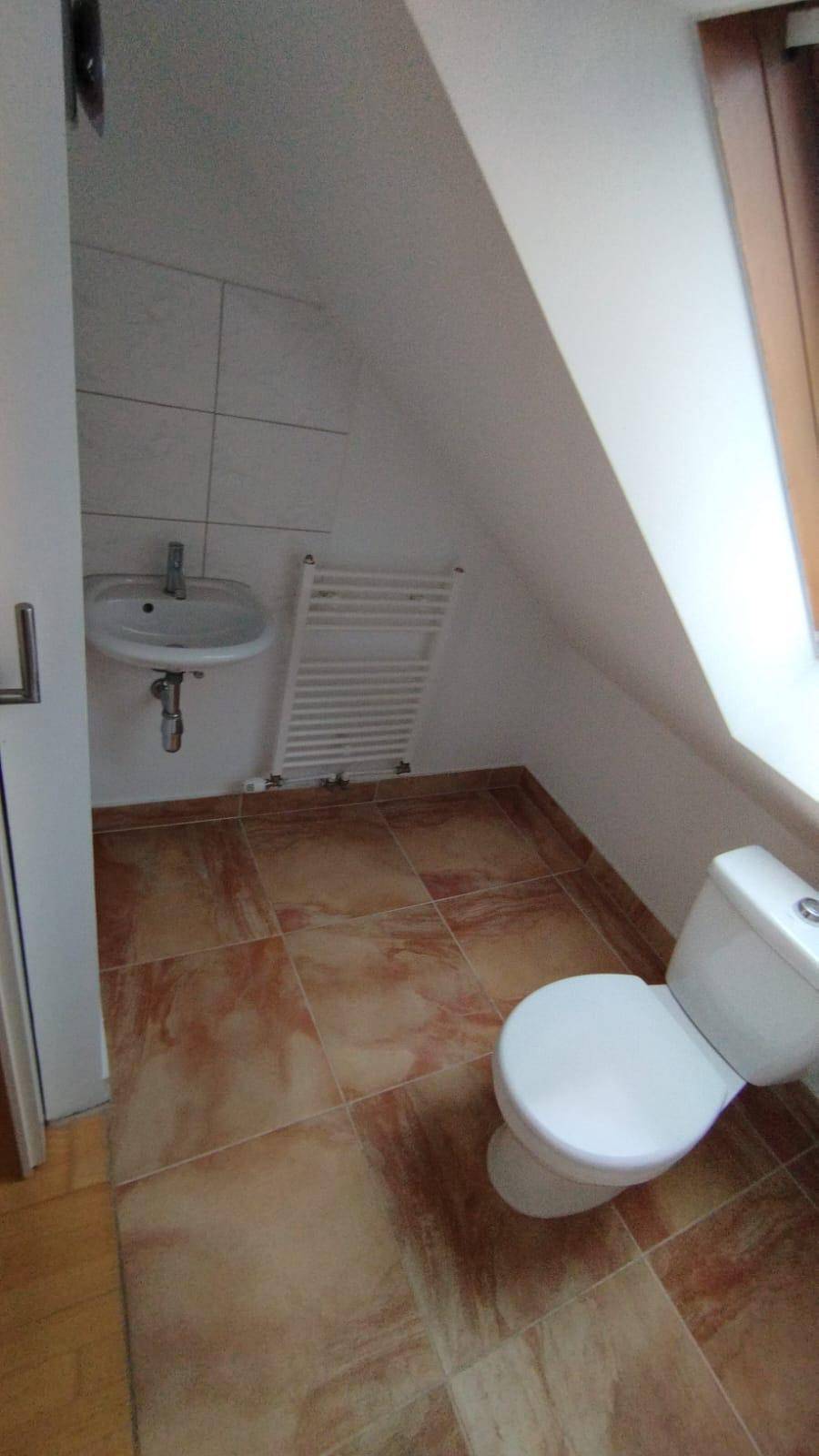 Dachgeschoss-Badezimmer mit WC, Waschbecken, beheiztem Handtuchhalter und Fliesenboden.