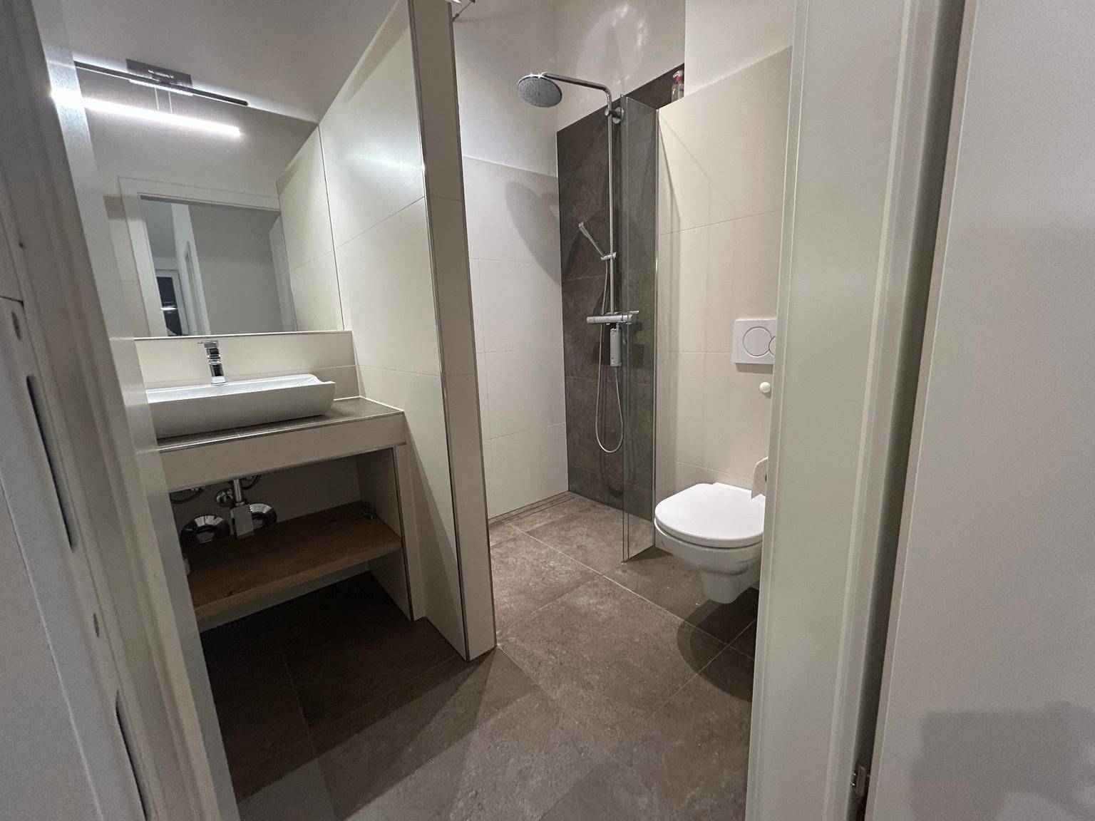 Modernes Badezimmer mit ebenerdiger Dusche, wandhängendem WC und stilvollem Waschbecken.