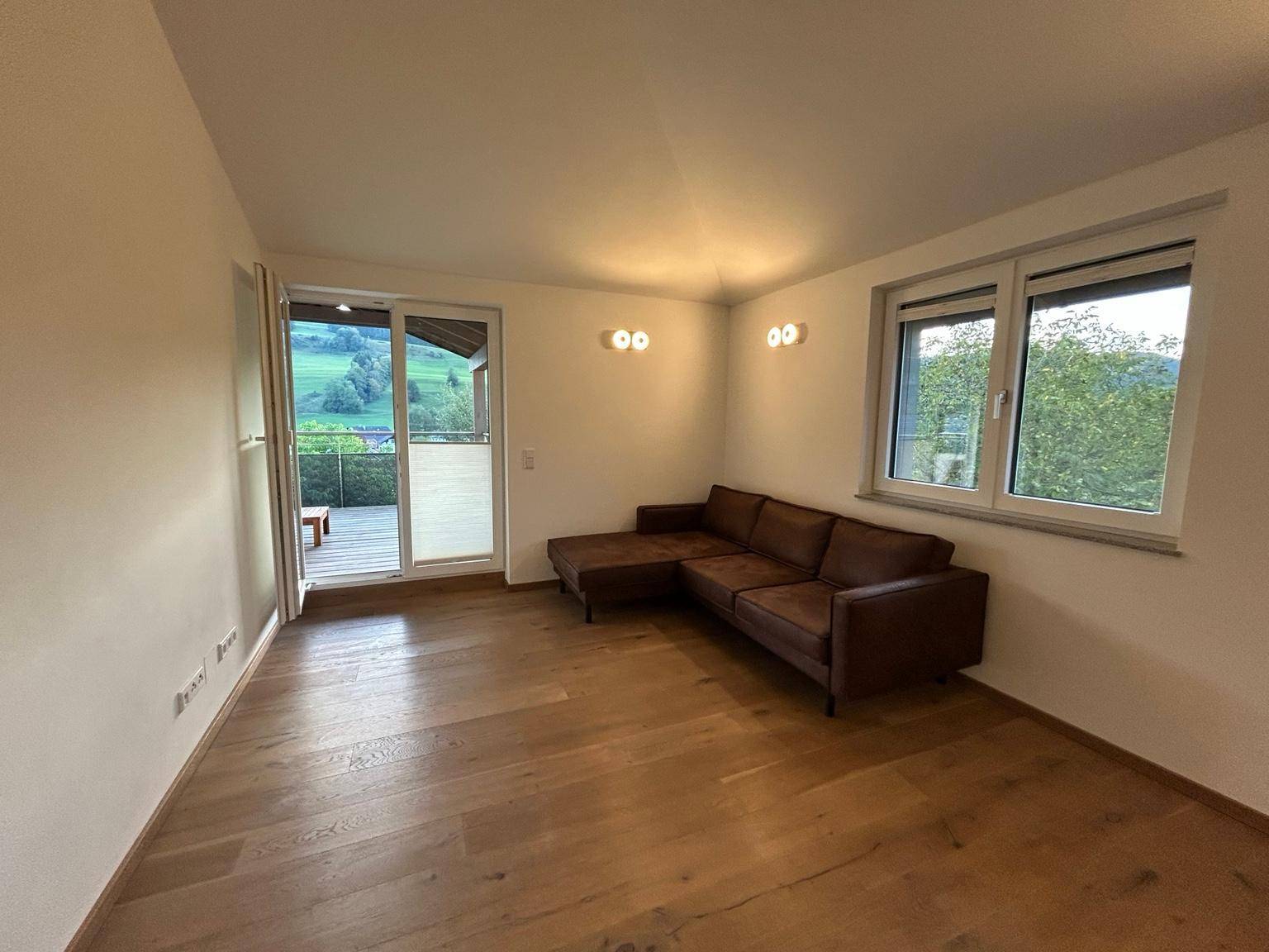 Helles Wohnzimmer mit Holzboden, gemütlichem Sofa und Zugang zu einem Außenbereich mit schöner Aussicht.