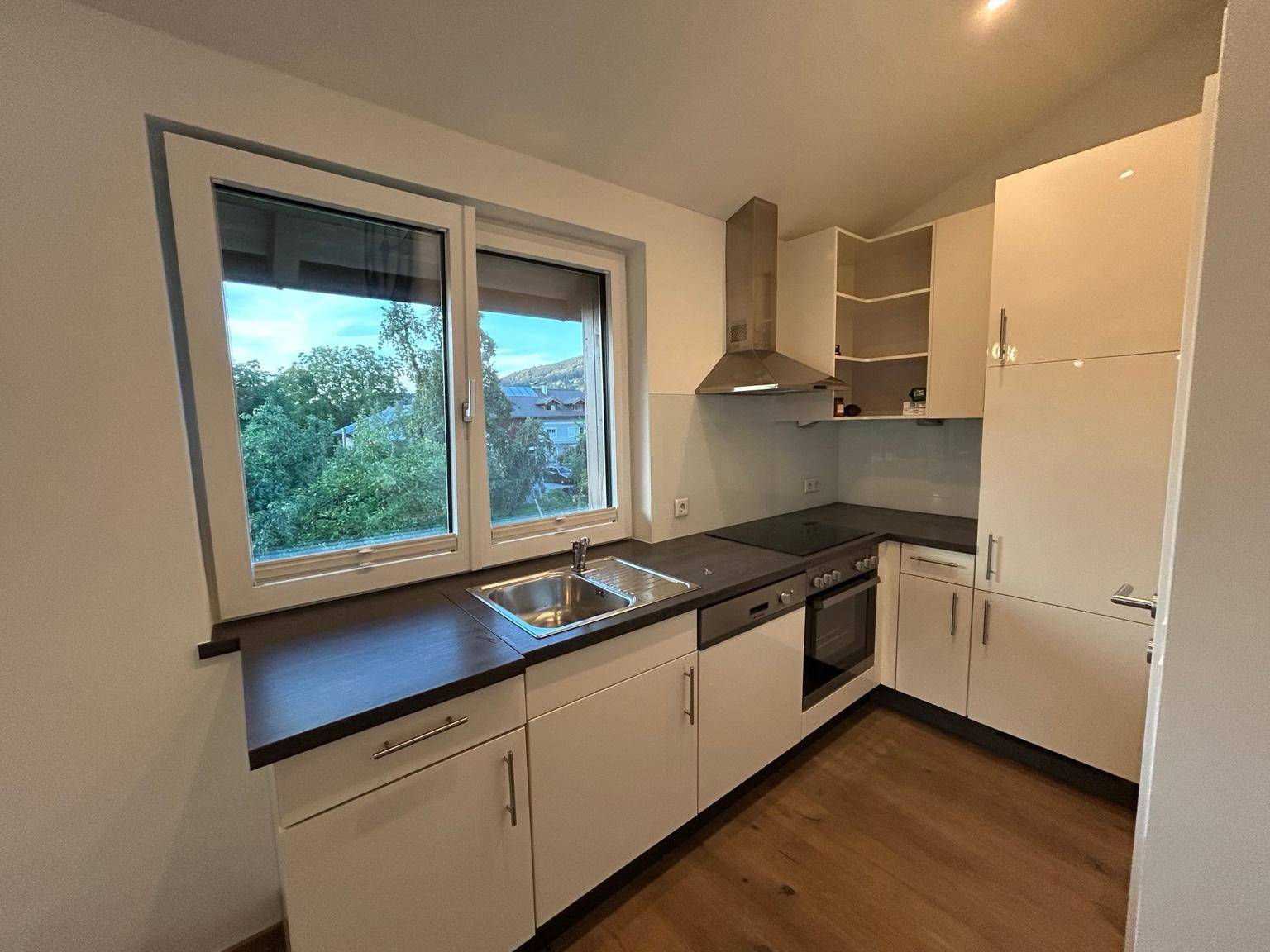 Moderne Küche mit weißen Schränken, dunkler Arbeitsplatte und Fenster mit Blick ins Grüne.