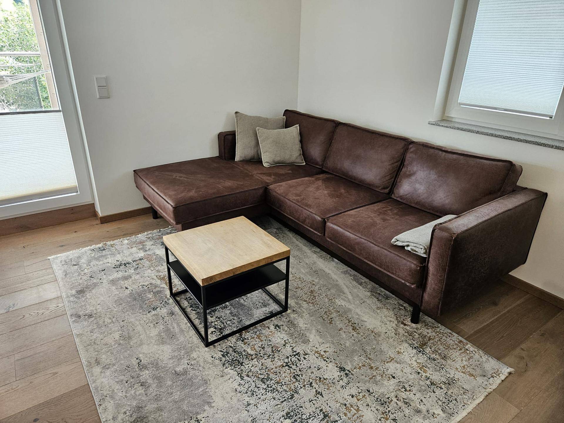 Gemütlicher Wohnbereich mit braunem Ecksofa, Couchtisch und hellem Teppich.