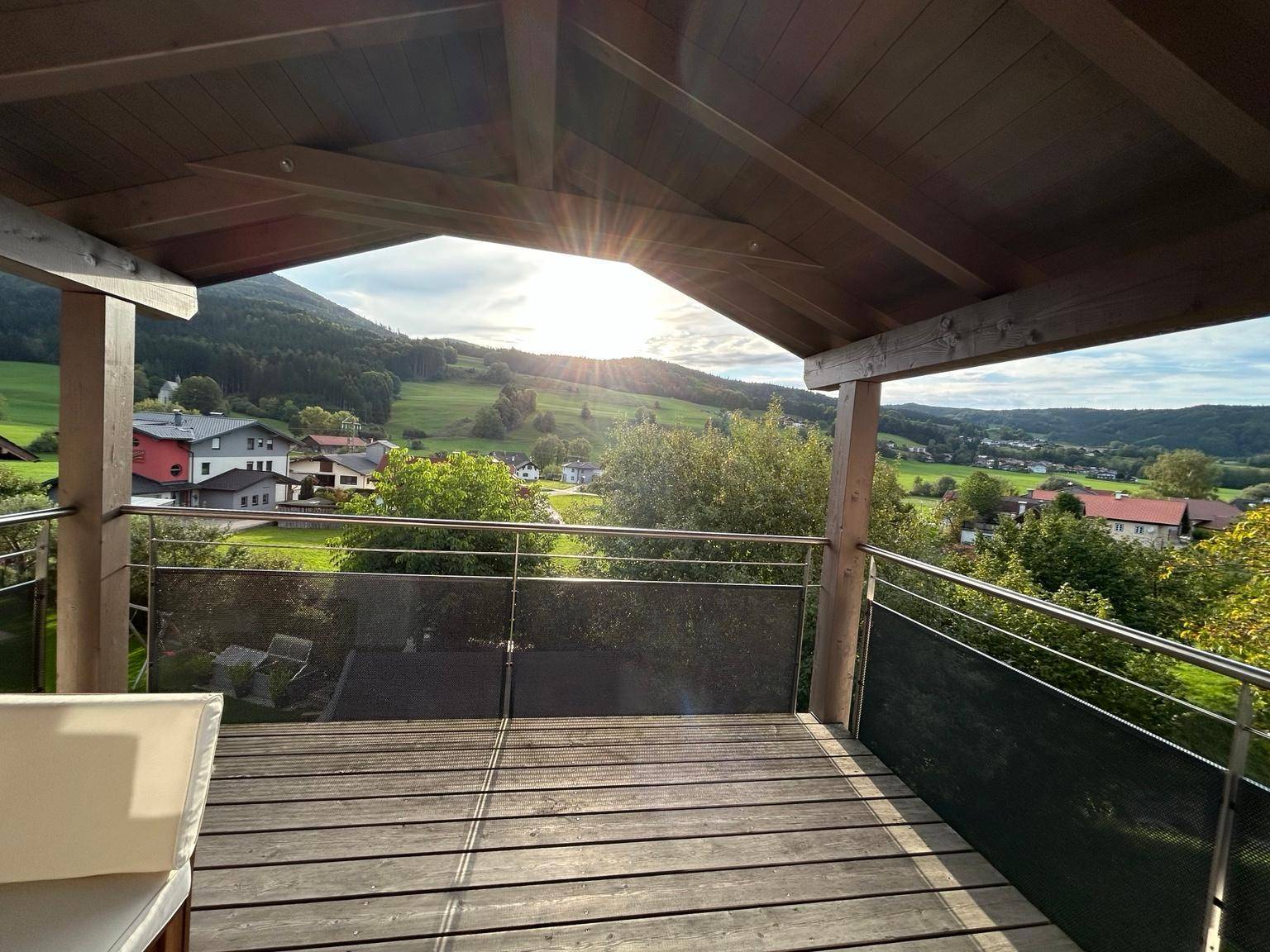 Überdachte Terrasse mit Holzboden und weitem Panoramablick über die grüne Hügellandschaft.