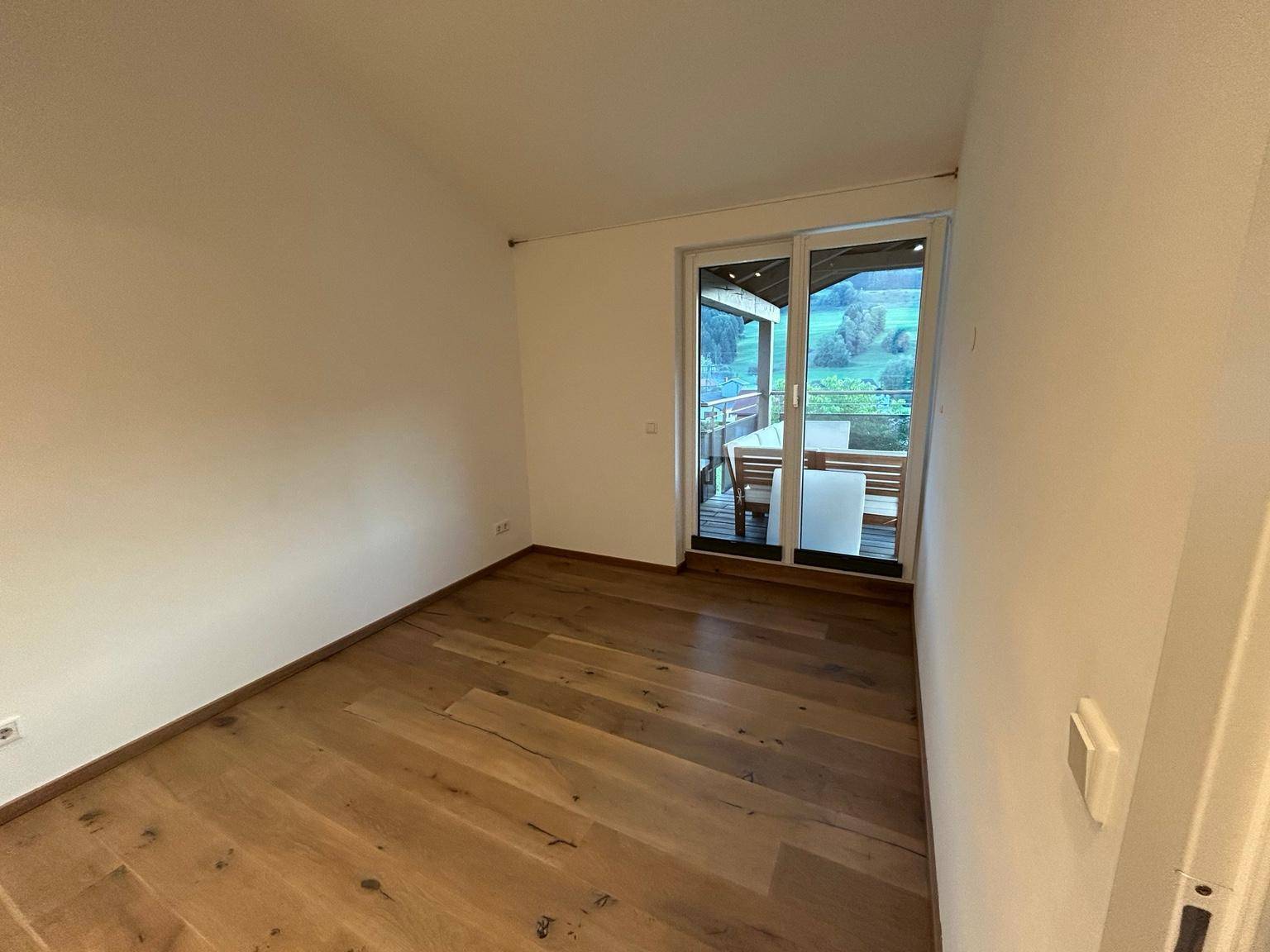 Leerer Raum mit Holzboden und Zugang zu einem Außenbereich mit Sitzgelegenheiten und schöner Aussicht.